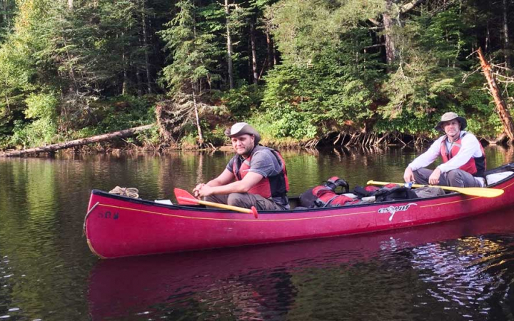 veterans smile at the camera while sitting in a canoe on an outward bound expedition